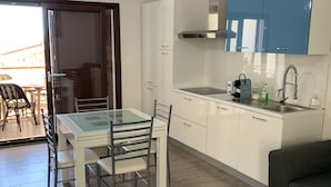 A modern kitchen with white cabinets, a blue upper cabinet, a stainless steel sink, and a glass-top dining table with chairs. - Modern apartment in the historic center of Orosei 70 M² - French Alps  (OROSEI)