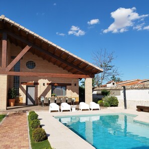 A poolside area with a brick building, outdoor seating, and a clear blue sky. - My favorite place (Torrejón del Rey)