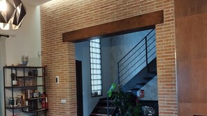 Un salon moderne avec des murs en briques apparentes, un escalier et un coin repas agrémenté d’un chemin de table rond en fibres tressées.