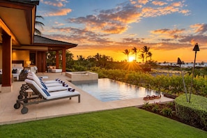 A resort with a swimming pool, lounge chairs, and a view of the sunset.