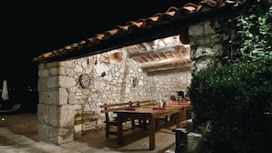 An outdoor stone building with a tiled roof, a wooden table, and benches. - Breathtaking villa with a private pool (Labin)