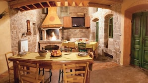A rustic stone kitchen with a wood-burning stove, a dining table set for four, and a television mounted above the stove. - Breathtaking villa with a private pool (Labin)