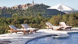 A poolside area with lounge chairs and a large umbrella, overlooking a hillside with buildings. - Breathtaking villa with a private pool (Labin)