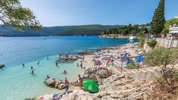 A coastal beach with clear waters, rocky terrain, and a few people swimming. - Breathtaking villa with a private pool (Labin)