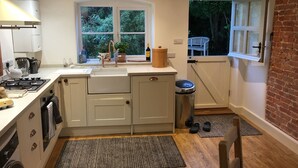 Een kleine keuken met een spoelbak, fornuis en een raam met uitzicht op groen.