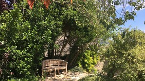Een houten bank in een tuin met weelderige begroeiing en een stenen muur op de achtergrond.