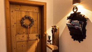 A wooden door with a wreath, a wall-mounted shelf with books, and a wall sconce.