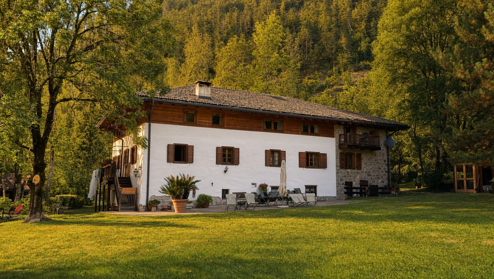 A two-story building with a white facade and wooden shutters, surrounded by a well-maintained lawn and dense forest.