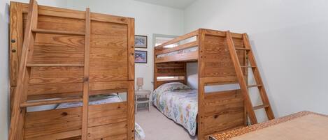 A room with two bunk beds, a small desk, and a chair.