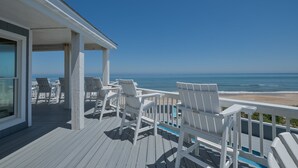 A wooden deck with white Adirondack chairs overlooking a beach and ocean. - 2065 - Sweet Home Carolina - Oceanfront Escape w/ Pool, Hot Tub & Views (Corolla)