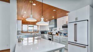 A modern kitchen with a large island, white cabinetry, stainless steel appliances, and pendant lighting. - 2065 - Sweet Home Carolina - Oceanfront Escape w/ Pool, Hot Tub & Views (Corolla)