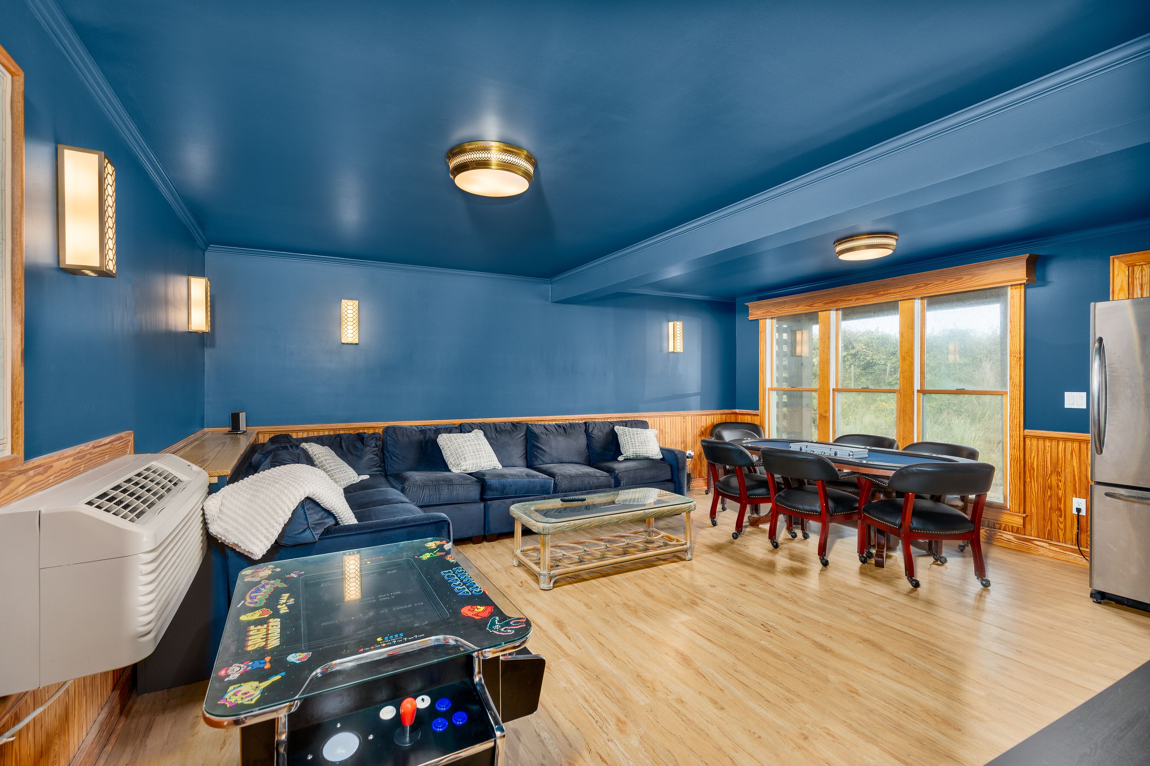 A room with a blue wall, a wooden floor, a sofa, a table, chairs, a heater, and a refrigerator.
