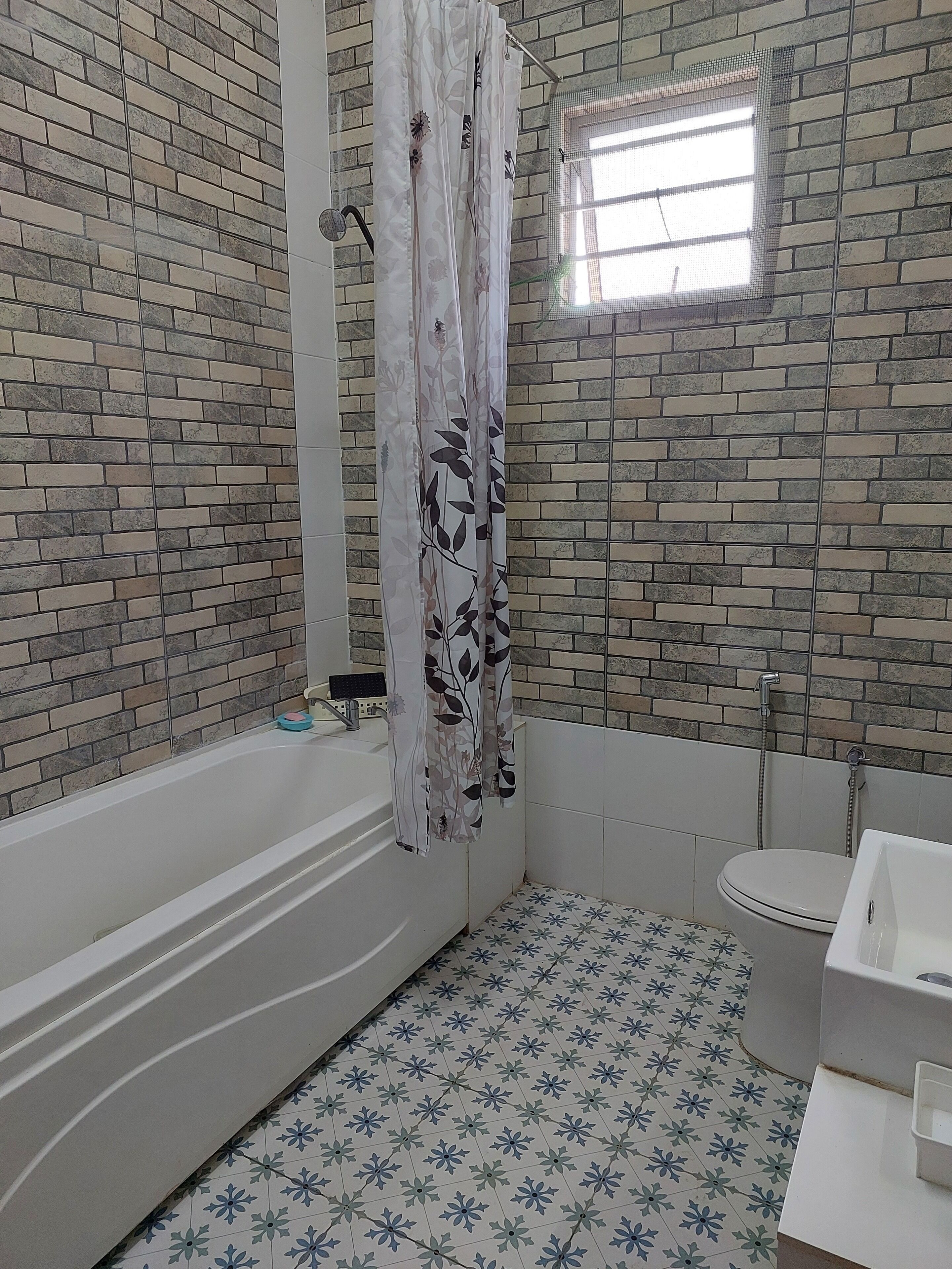 A bathroom with a brick-patterned wall, a bathtub, a toilet, and a shower.