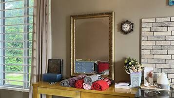 A room with a wooden desk, a mirror, a clock, a brick-patterned wall, and a window with curtains.