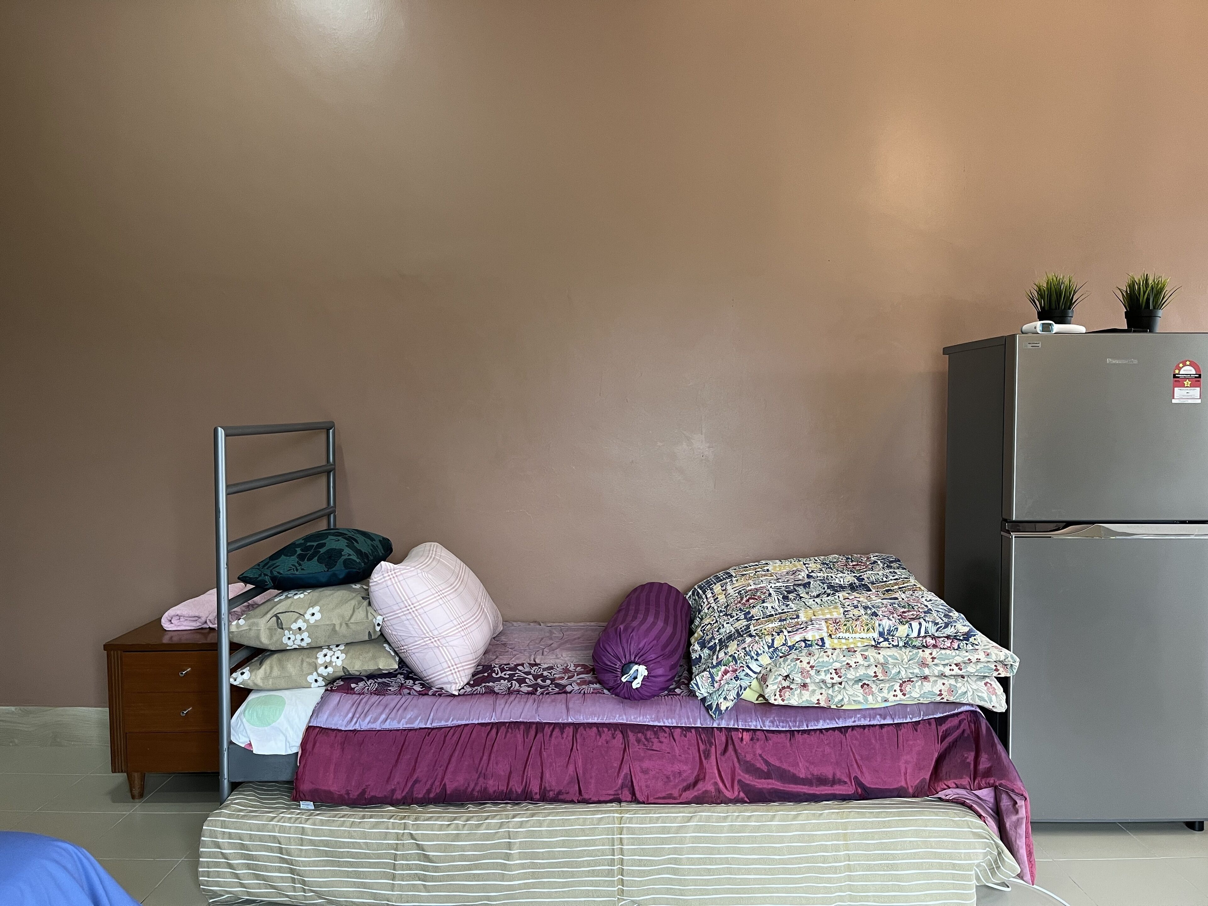 A bedroom with a bed, a nightstand, a dresser, and a refrigerator.