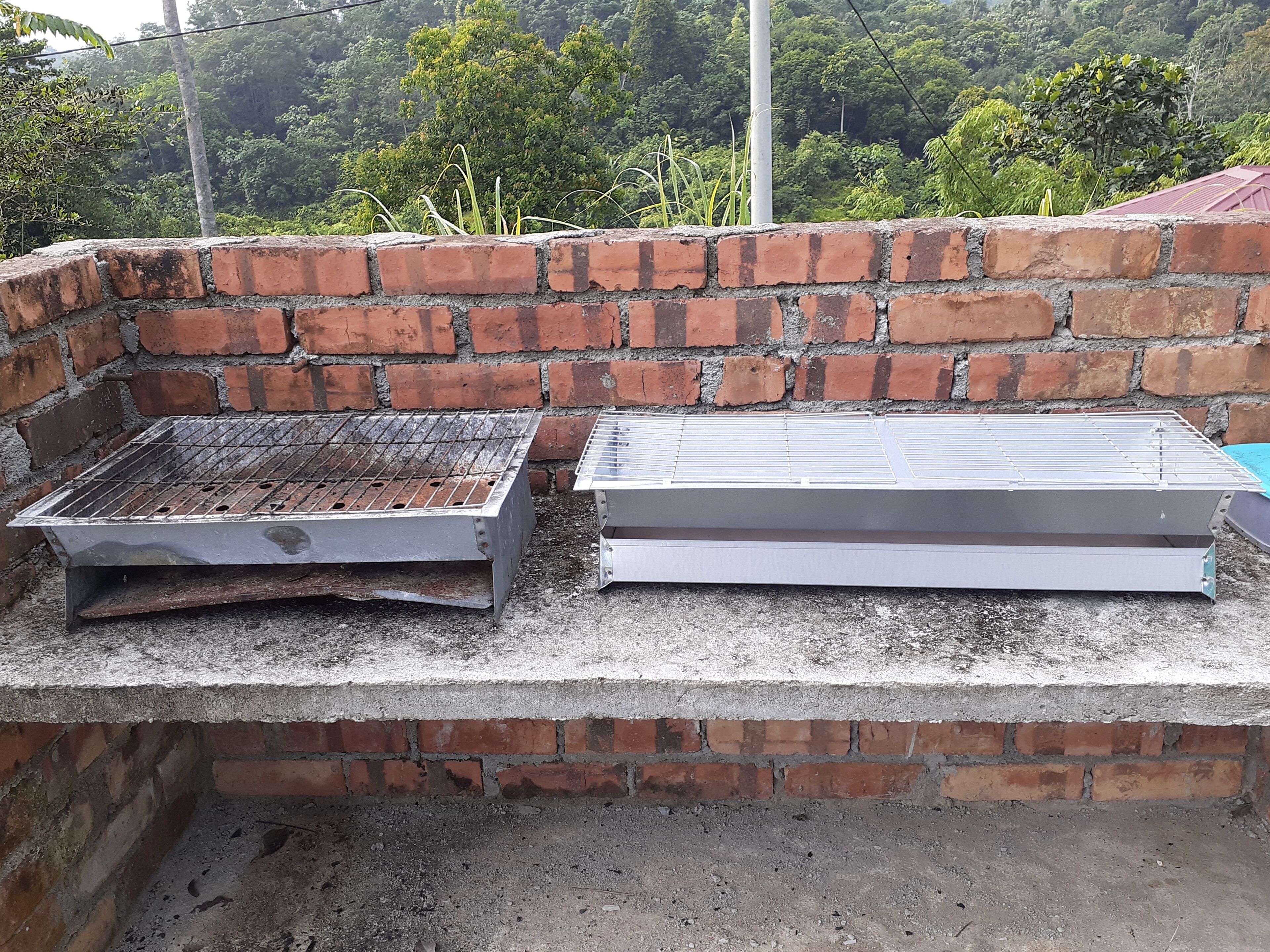 A brick barbecue grill with a metal grate and a flat metal surface, likely for grilling or cooking, set against a brick wall.