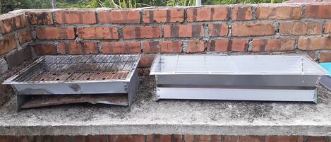 A brick barbecue grill with a metal grate and a flat metal surface, likely for grilling or cooking, set against a brick wall.