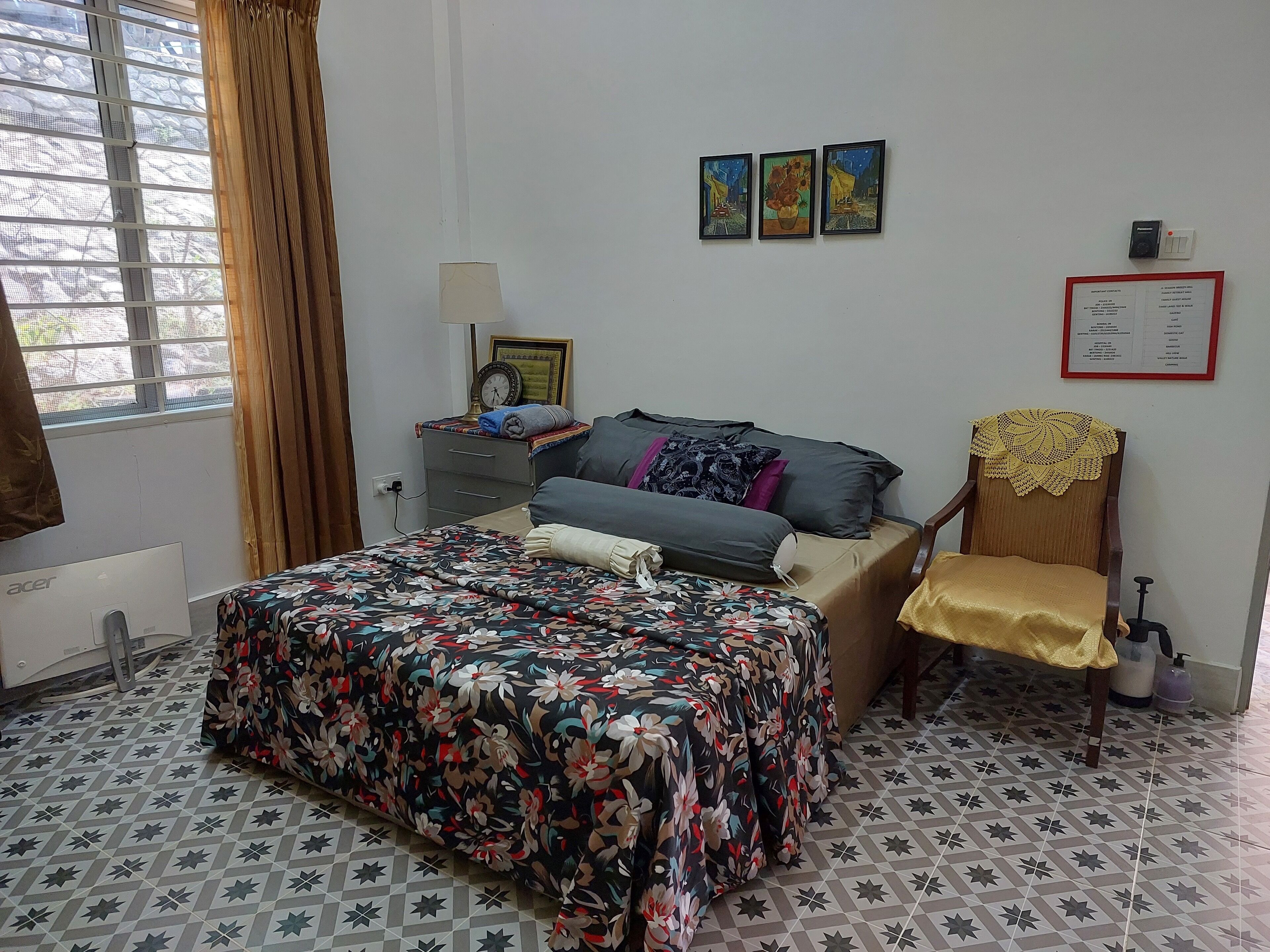 A bedroom with a bed, a chair, a nightstand, a window, and a wall with three framed pictures.