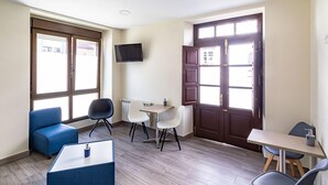 Una habitación con un sofá azul, una mesita, un televisor montado en la pared y una puerta con ventanal.