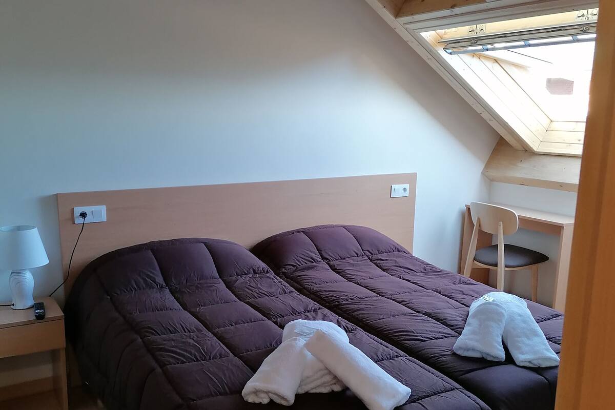 Un dormitorio con dos camas, una mesita de noche con lámpara y un tragaluz.