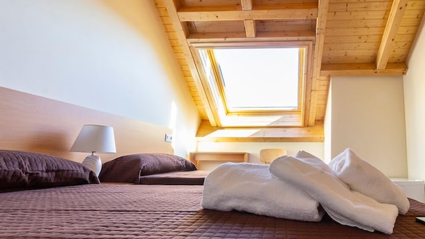 Un dormitorio con techo inclinado, un tragaluz, cama con ropa de cama marrón, lámpara de noche y una pila de toallas blancas.