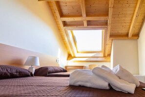 Une chambre avec un plafond en pente, un puits de lumière, un lit avec une literie marron, une lampe de chevet et une pile de serviettes blanches.