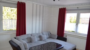 Ein Wohnzimmer mit grauem Sofa, einem schwarzen Couchtisch und roten Vorhängen.