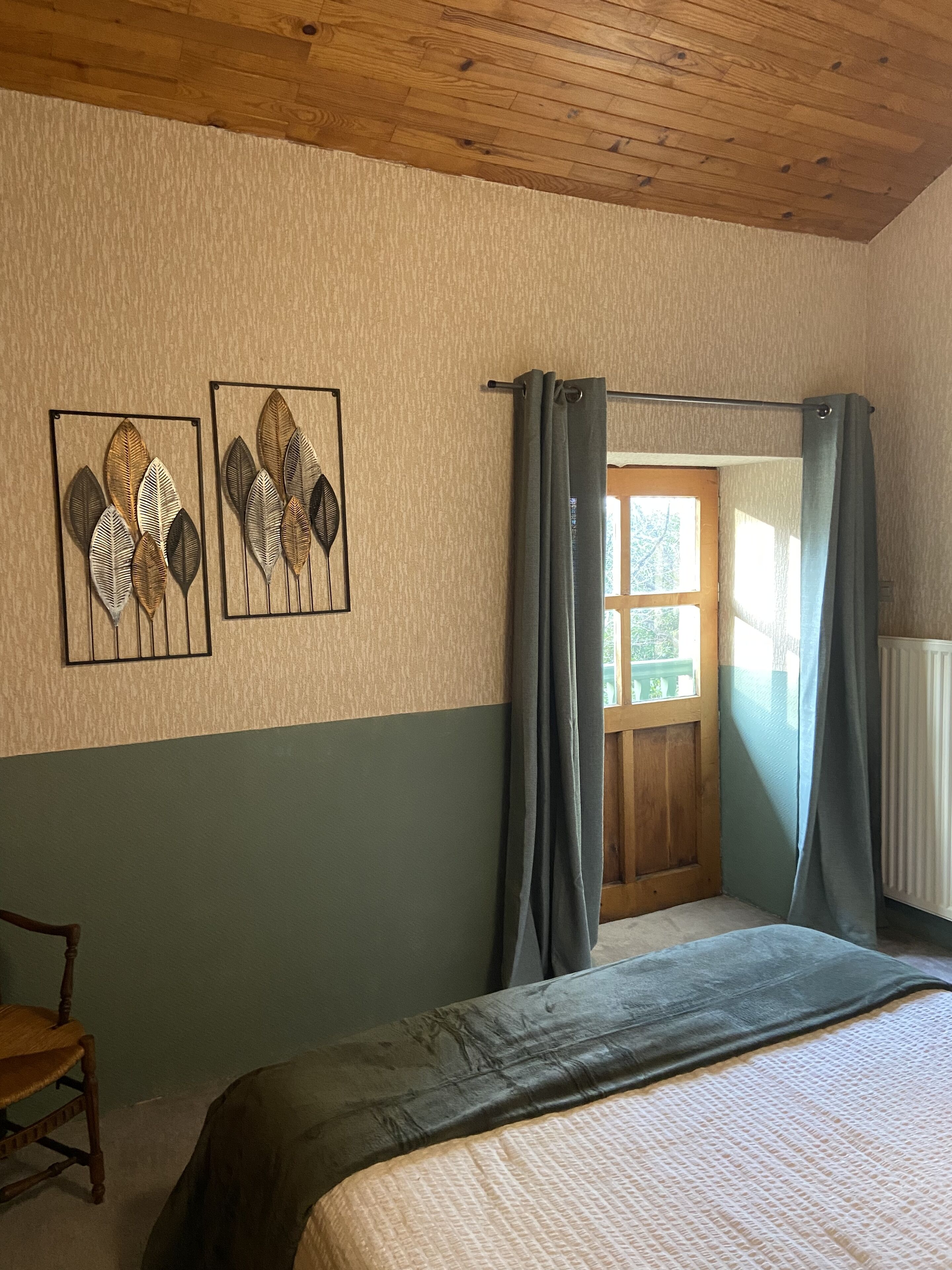 Een slaapkamer met een bed, een stoel, een raam met gordijnen en twee decoratieve wandpanelen.