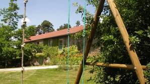 Un ensemble de balançoires en bois avec des cordes, une pelouse verdoyante et une maison avec un toit rouge en arrière-plan.