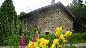 Un bâtiment en pierre avec un toit rouge, entouré d’une végétation luxuriante et de différentes sortes de fleurs.