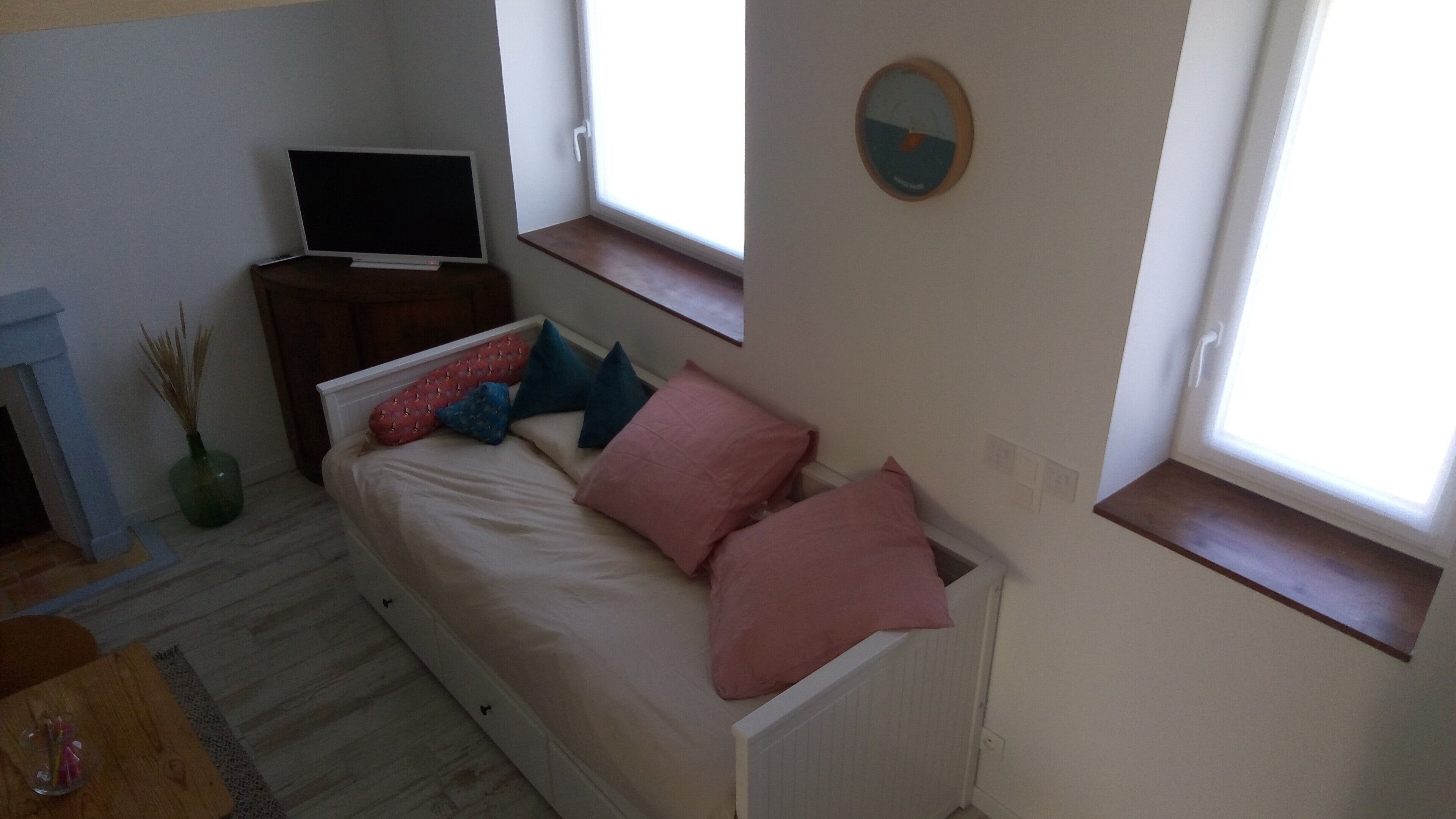 Pieni, viihtyisä huone, jossa on sänky, televisio, kello ja ikkuna.