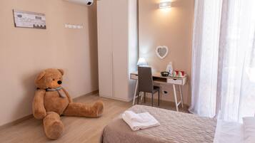 Habitación de hotel con cama, escritorio y silla, un oso de peluche, y una lámpara de pared.