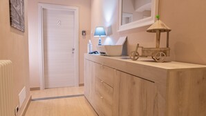 A hallway with a wooden cabinet, a small lamp, a bicycle-shaped decoration, and a door with the number 2. - Le Camere di Teo 2 (La Spezia)