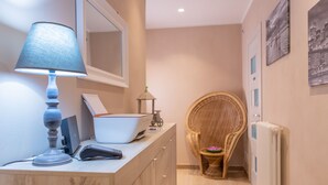 A bathroom with a wooden vanity, a mirror, a lamp, a wicker chair, and a radiator. - Le Camere di Teo 2 (La Spezia)