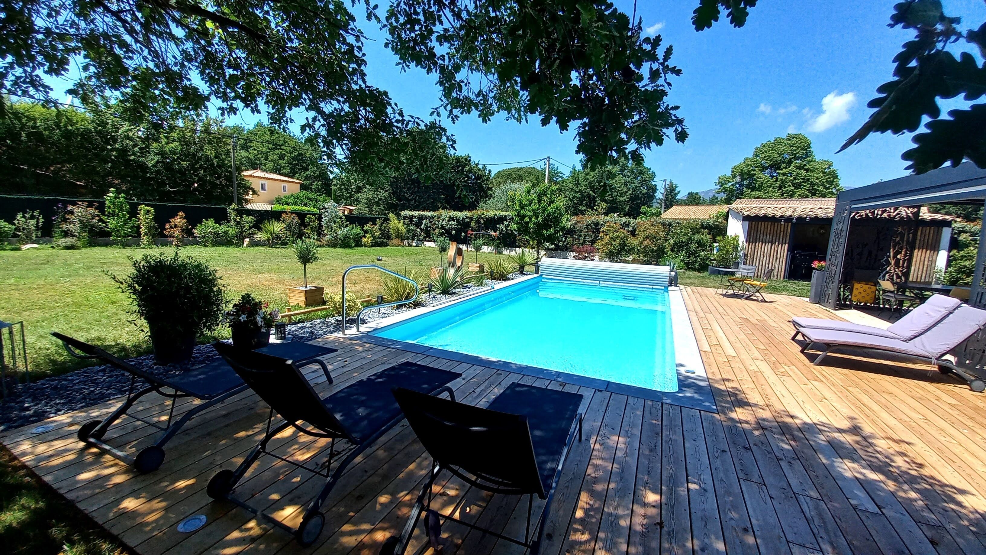 A wooden deck with a swimming pool, lounge chairs, and a small garden area.