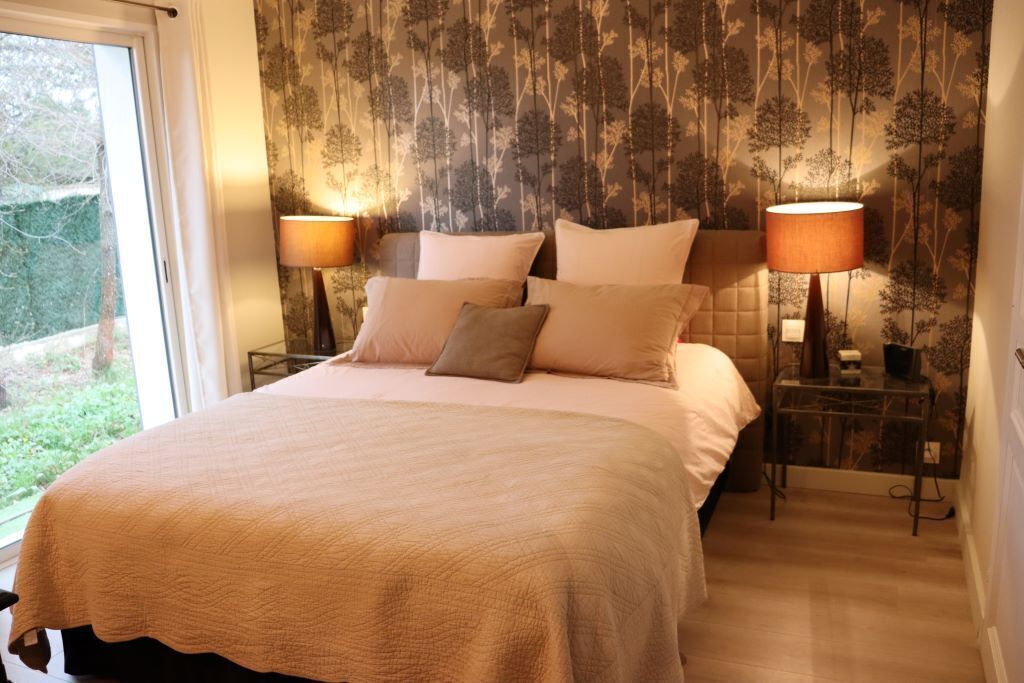 A bedroom with a large bed, two bedside lamps, and a window with a view of greenery.