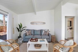 Ein modernes Wohnzimmer mit grauem Sofa, Korbstühlen, einem weißen Couchtisch und einer großen Topfpflanze.