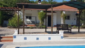 Un espacio de estar al aire libre techado con piscina, patio y un edificio con techo de tejas.