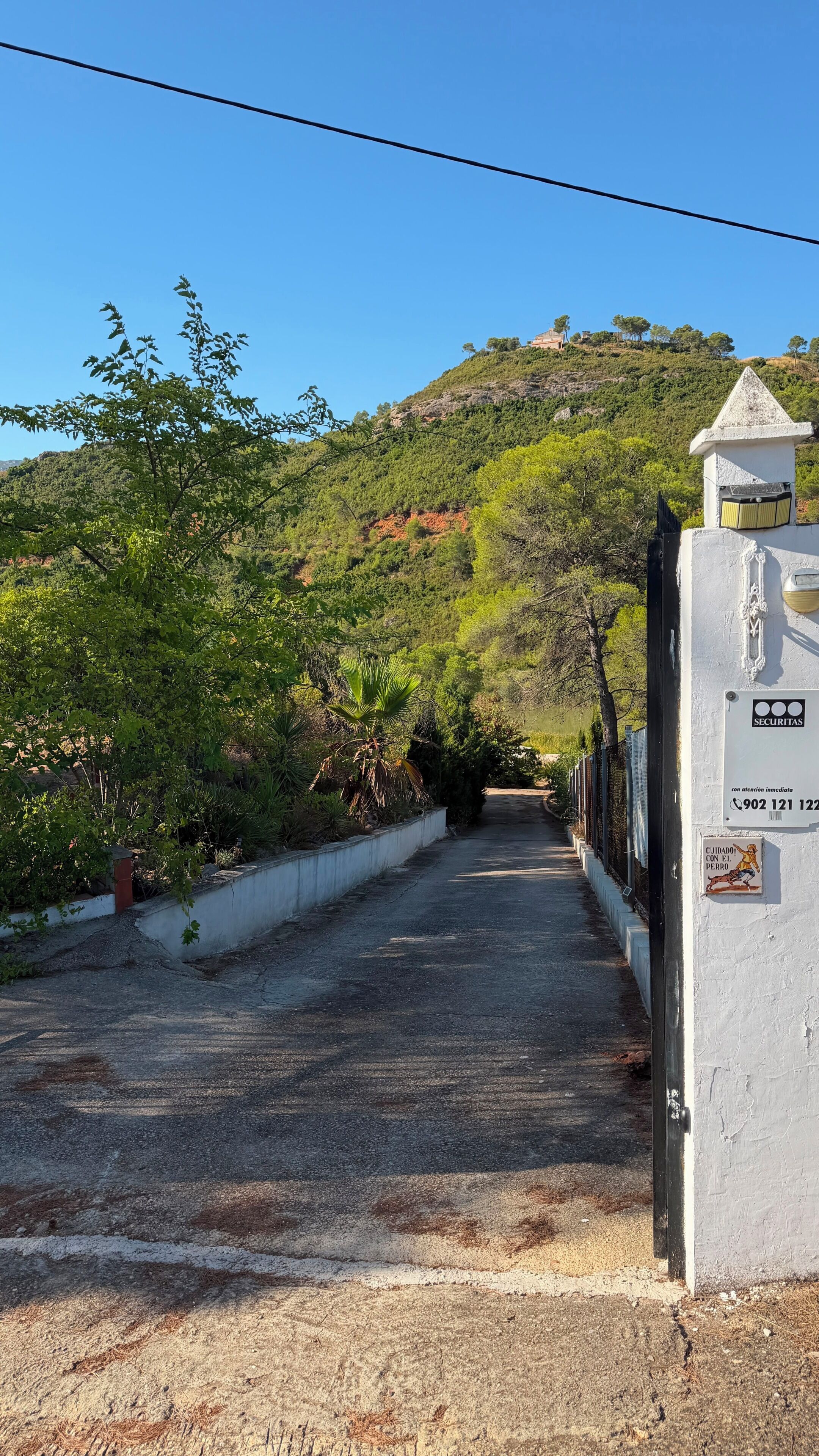 Un chemin menant à un bâtiment sur lequel on peut voir un panneau indiquant qu’il est sous surveillance et un numéro de téléphone à contacter.