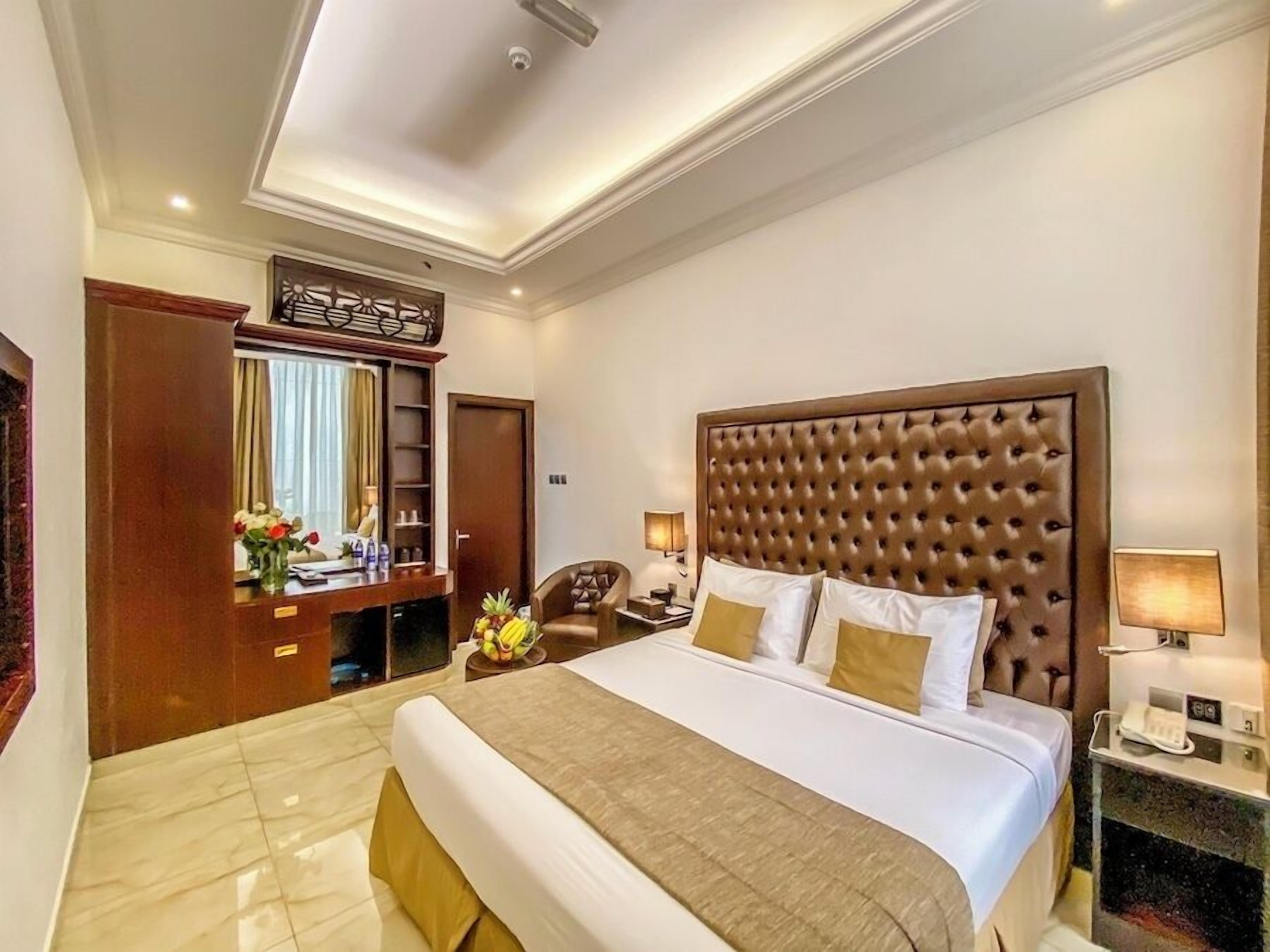Habitación de hotel con una cama grande, cabecera de madera, escritorio con espejo y un pequeño rincón de descanso.