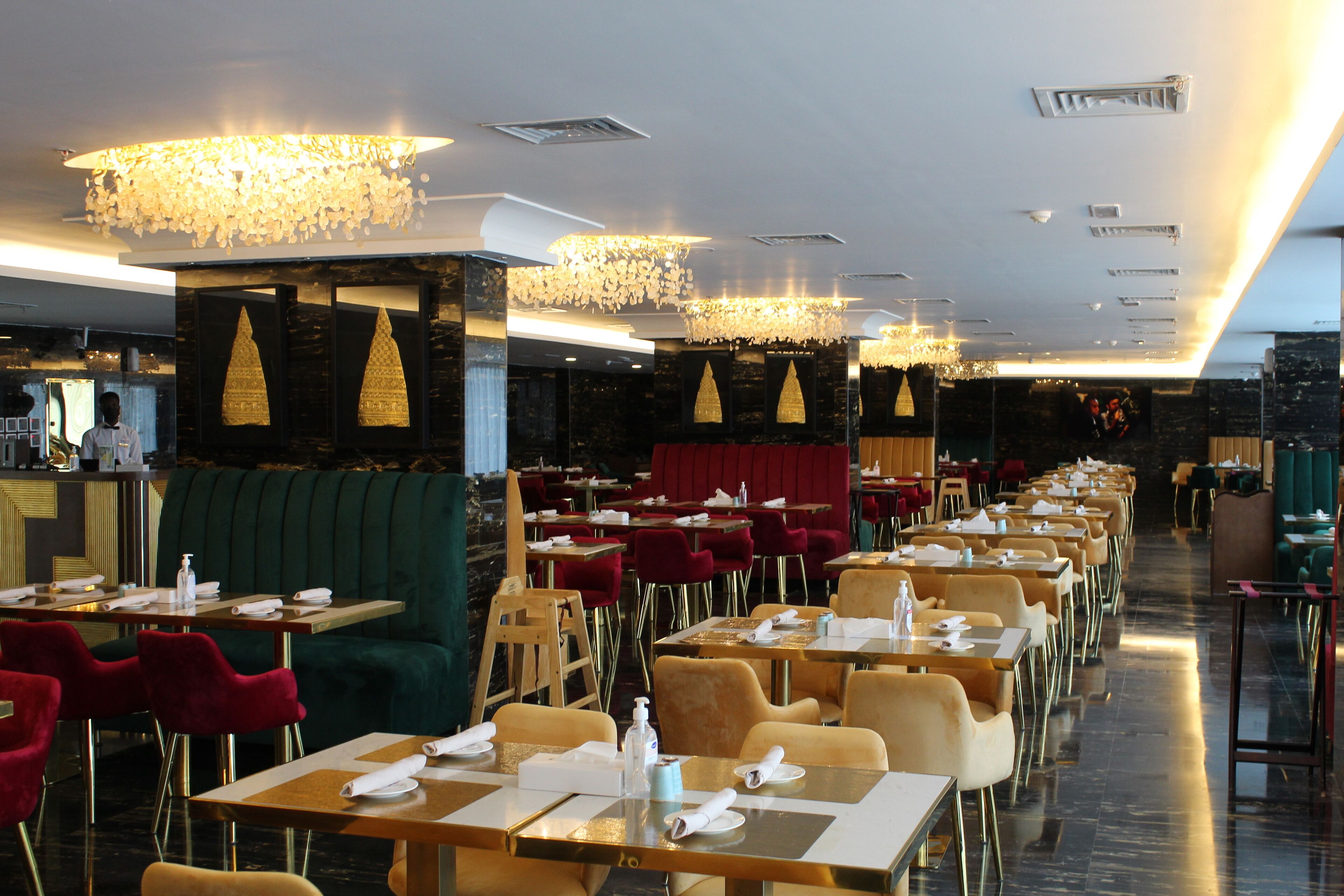 A restaurant with multiple dining tables and chairs, a bar area, and a stage with red curtains.