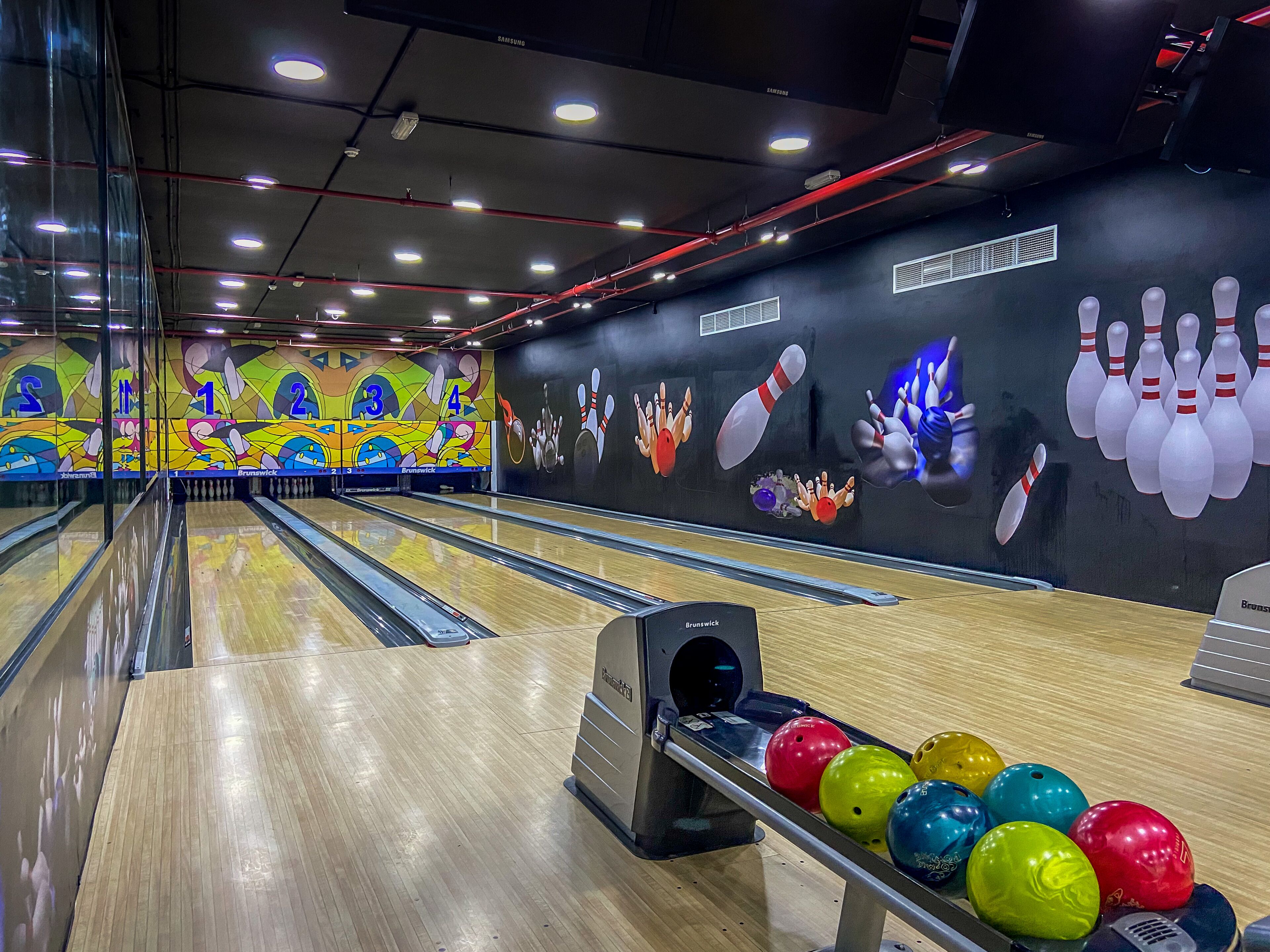 Bolera con varias pistas, bolas de bolos coloridas y un mural con bolos y números.
