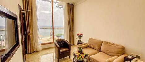 Un salon avec un canapé, un fauteuil et un téléviseur. Une grande fenêtre offre une vue sur la mer.