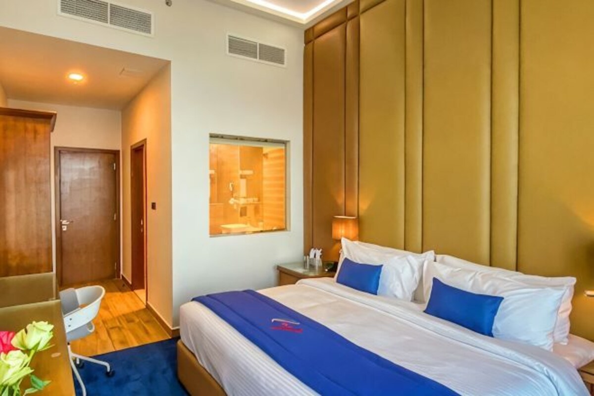 Una habitación de hotel con una cama grande, un escritorio con una silla, una ventana y una puerta.