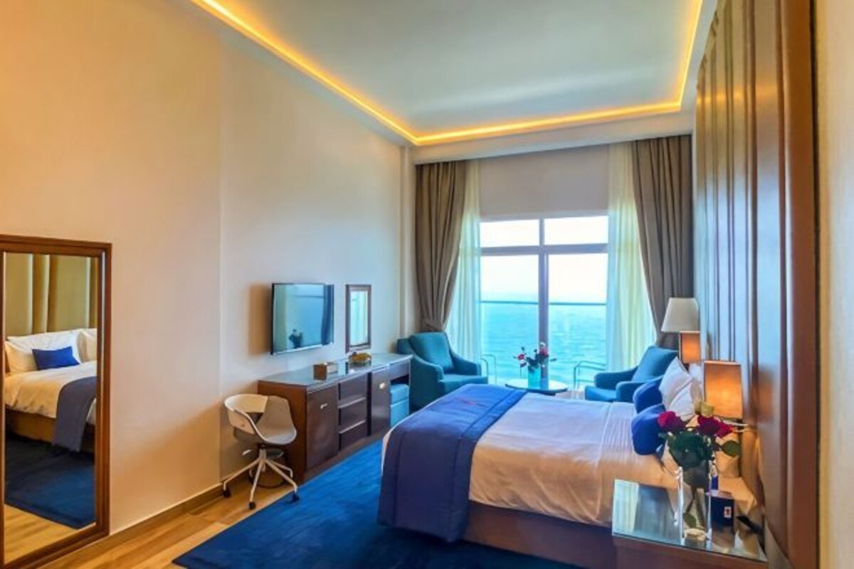 Habitación de hotel con cama, escritorio, silla, televisión y vista al mar.