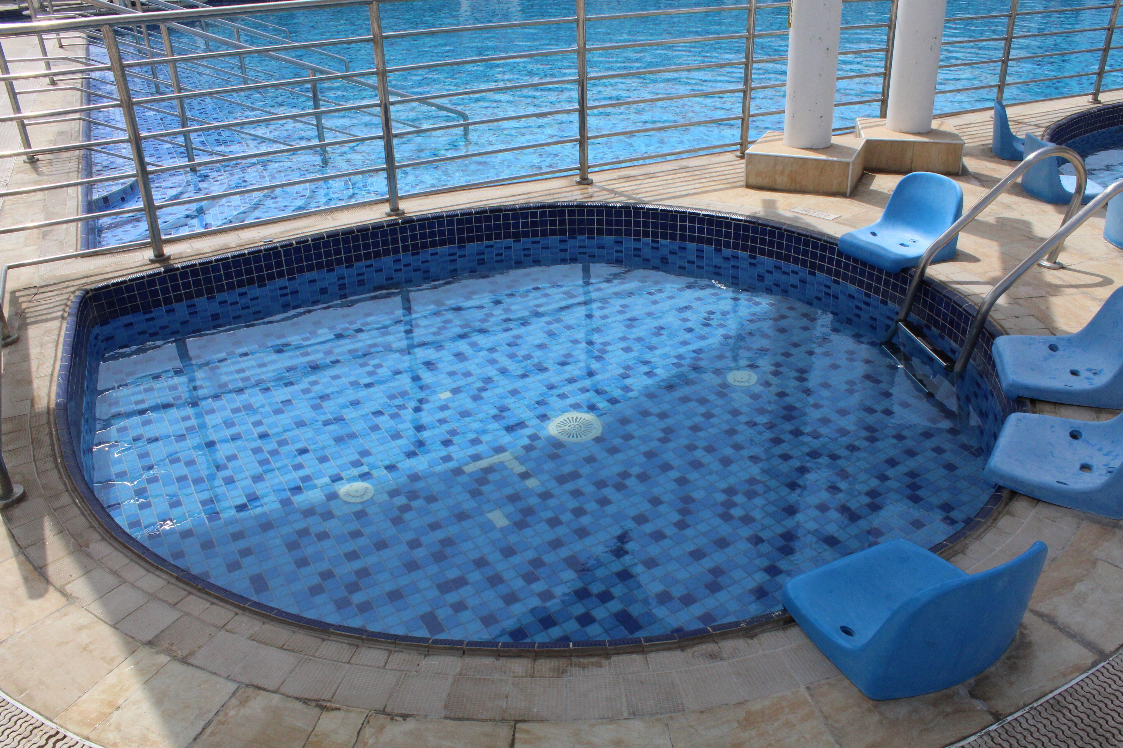 A circular pool with blue mosaic tiles and a metal railing.