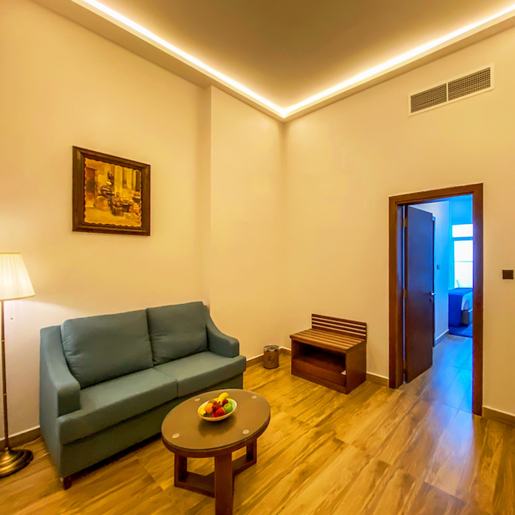 A living room with a sofa, a small table with fruit, a bench, and a door leading to another room.
