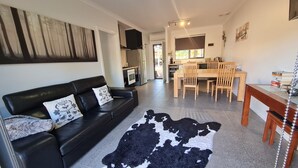A modern living room with a black leather sofa, a cowhide rug, and a dining area with wooden chairs and a table.