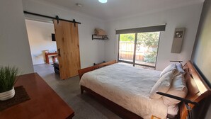 A bedroom with a bed, a wooden door, a small table, and a window with a view of the outdoors.