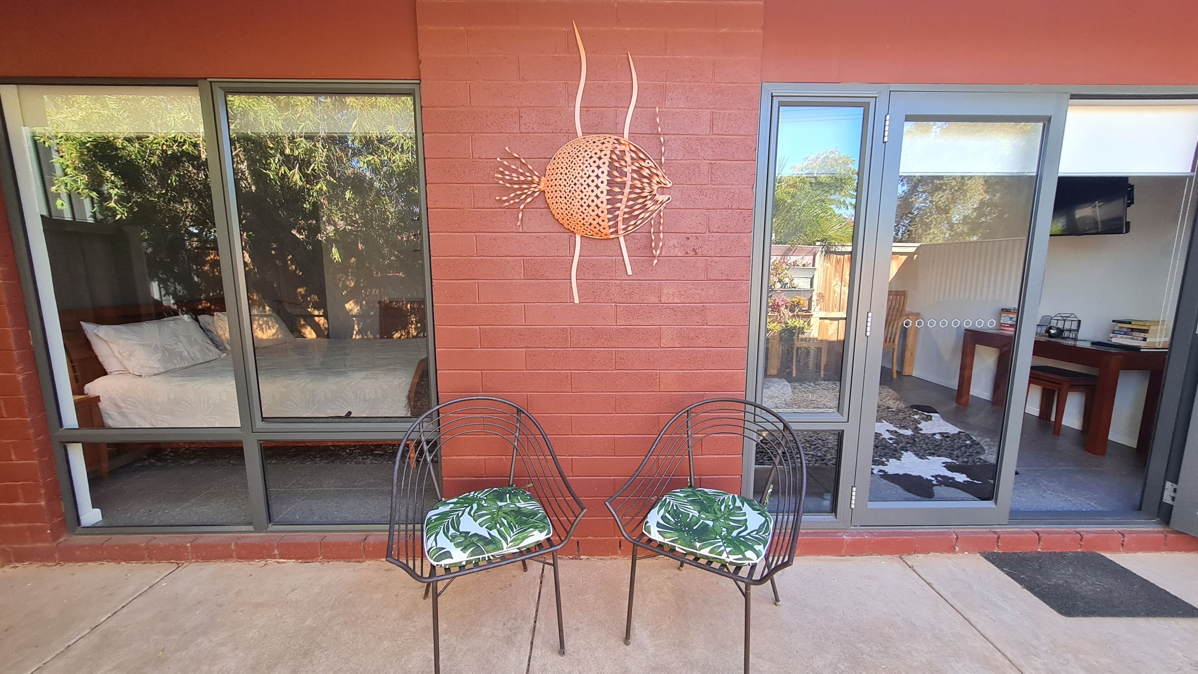 Une pièce comprenant un lit, une porte-fenêtre coulissante et deux chaises ornées d’un motif de feuilles.